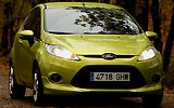 Ford Fiesta. Modelo 2009. Imagen. Lateral frontal. Coche parado. Carretera. Luces faros en on. Color verde squeeze.