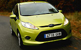 Ford Fiesta. Modelo 2009. Imagen. Lateral frontal. Coche en movimiento. Luces faros en on. Carretera. Color verde squeeze.