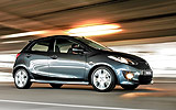 Mazda2. Modelo 2008. Kit deportivo. Imagen. Exterior. Lateral- frontal. Coche en movimiento. Carretera. Color Brilliant Black.