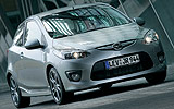 Mazda2. Modelo 2009. Kit deportivo. Imagen. Exterior. Lateral frontal. Coche parado. Carretera. Gris.