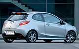 Mazda2. Modelo 2009. Kit deportivo. Imagen. Exterior. Posterior lateral. Coche parado. Carretera. Luces pilotos en on. Gris.