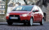 Mitsubishi Colt. Modelo 2009. 3 puertas. Imagen. Exterior. Frontal lateral. Coche parado. Carretera. Rojo Cranberry.