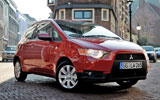 Mitsubishi Colt. Modelo 2009. 3 puertas. Imagen. Exterior. Lateral frontal. Coche parado. Carretera. Rojo Cranberry.
