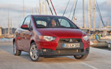 Mitsubishi Colt. Modelo 2009. 3 puertas. Imagen. Exterior. Lateral frontal. Coche parado. Carretera. Rojo Cranberry.