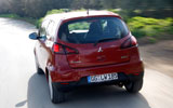 Mitsubishi Colt. Modelo 2009. 3 puertas. Imagen. Exterior. Lateral posterior. Coche en movimiento. Carretera. Rojo Cranberry.