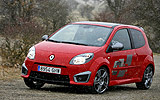 Renault Twingo RS. Modelo 2009. Imagen. Frontal lateral. Coche en movimiento. Carretera en curva. Luces faros en on. Rojo.