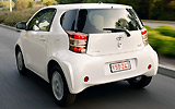 Toyota iQ. Modelo 2009. Imagen. Lateral posterior. Coche en movimiento. Carretera. Blanco.