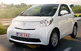 Toyota iQ. Modelo 2009. Imagen. Frontal lateral. Coche en movimiento. Carretera. Blanco.