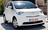Toyota iQ. Modelo 2009. Imagen. Lateral frontal. Coche parardo. Carretera. Blanco.