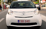 Toyota iQ. Modelo 2009. Imagen. Frontal. Coche en movimiento. Carretera. Blanco.