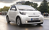 Toyota iQ. Modelo 2009. Imagen. Lateral frontal. Coche en movimiento. Carretera. Blanco.