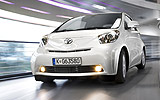 Toyota iQ. Modelo 2009. Imagen. Frontal lateral. Coche movimiento. Carretera. Luces antiniebla. Blanco.