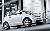 Toyota iQ. Modelo 2009. Imagen. Lateral frontal. Coche parado. Carretera en pendiente. Blanco.