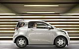 Toyota iQ. Modelo 2009. Imagen. Lateral. Coche en movimiento. Blanco.