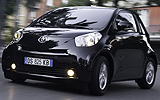 Toyota iQ. Modelo 2009. Imagen exterior. Frontal lateral. Movimiento. Carretera. Negro.