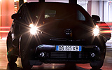 Toyota iQ. Modelo 2009. Imagen exterior. Frontal. Movimiento. Carretera. Negro. Faros encendidos.