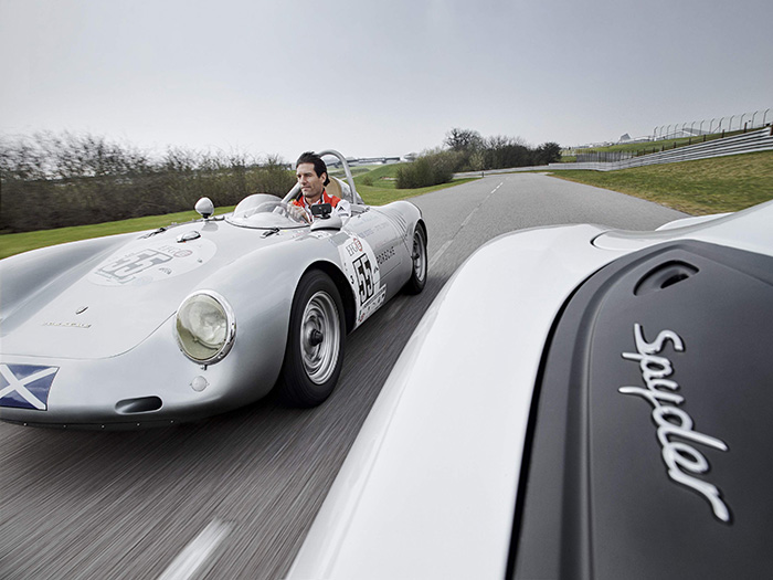 Mark Webber pilota un 550A (no muy en serio, va sin casco) siguiendo a un Boxster Spyder actual, en las pistas de pruebas que Porsche tiene junto al circuito británico de Silverstone. A pesar de la cruz escocesa, la unidad pertenece actualmente al taller del ex-piloto americano Bob Estes de Beverly Hills (California), como puede leerse (aumentando la foto) en la portezuela.