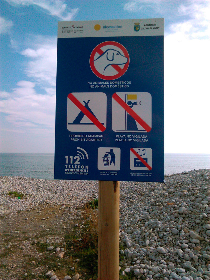 La dejadez del mantenimiento de la carretera contrasta con el cartel municipal: aunque la playa sea en realidad una gravera (se alterna con tramos de arena) se especifican todas las prohibiciones: animales domésticos (un tanto excesiva, me parece), acampar, tirar basura fuera de los recipientes adecuados, poner música a volumen excesivamente elevado, y una advertencia (no hay banderas de peligro ni vigilante con megáfono).