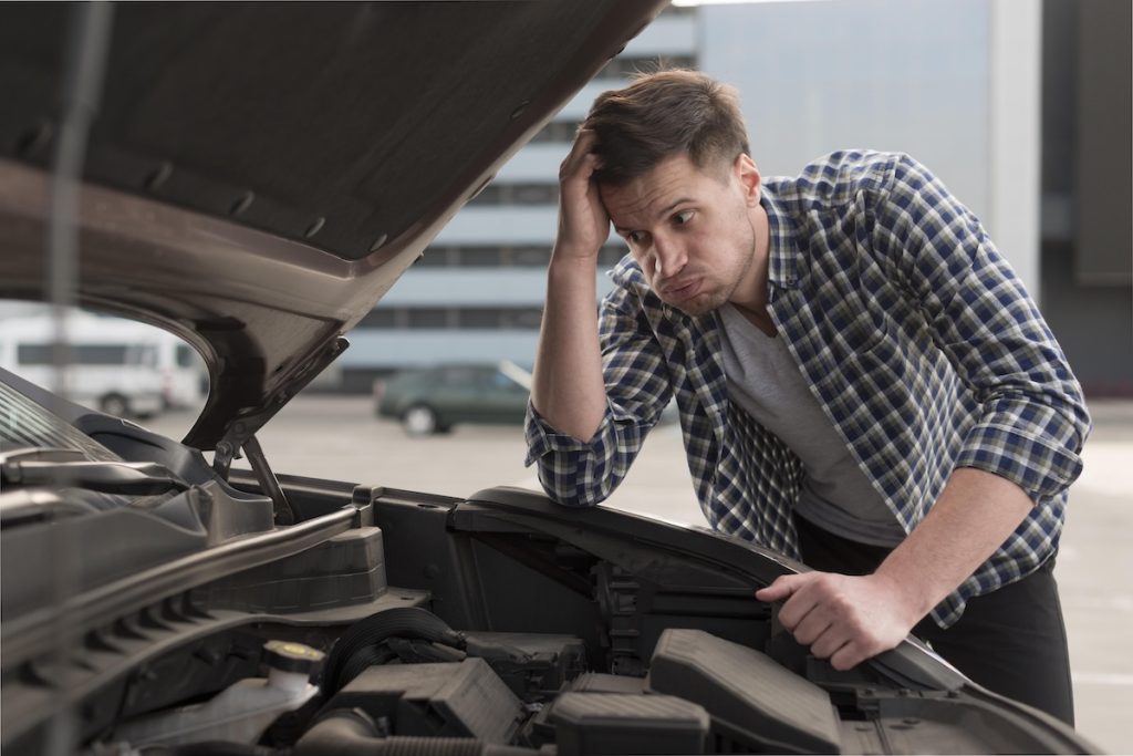 Joven conductor revisando el motor de su coche averiado por un mal uso