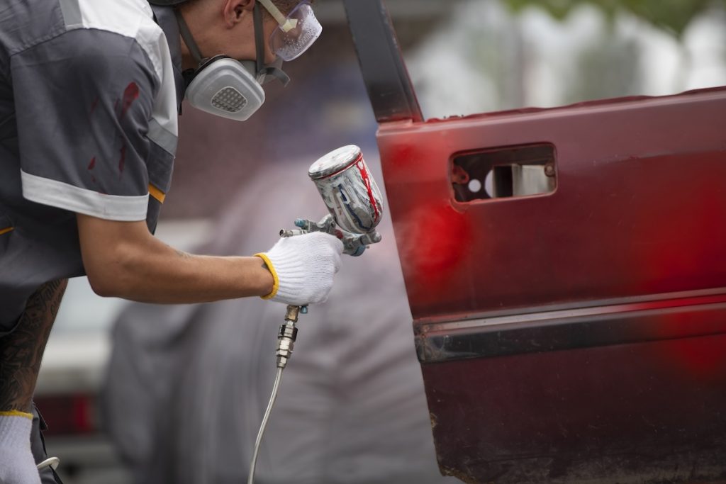 Trabajador de un taller de pintura dando un nuevo color rojo al coche
